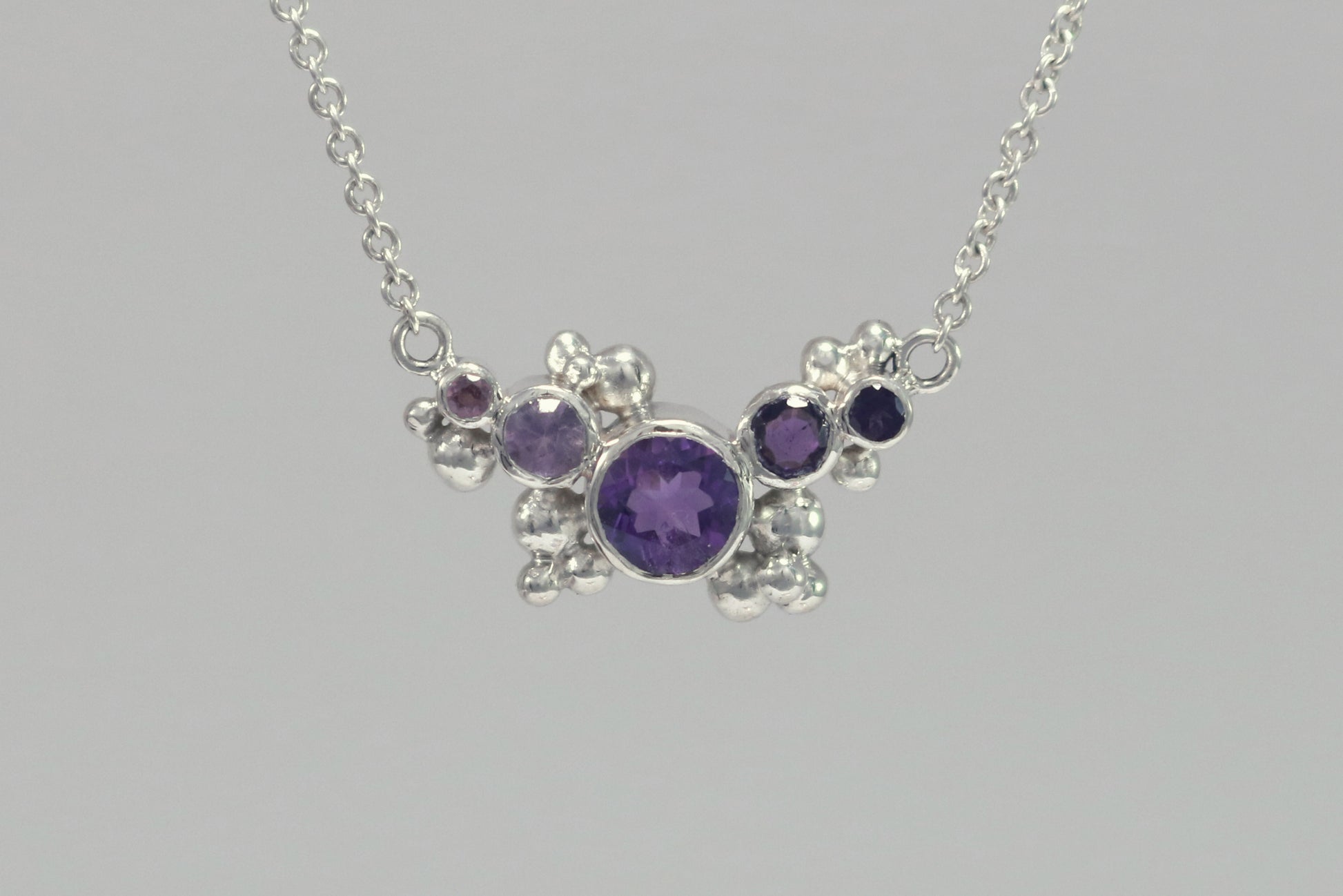 Different shades of round amethyst stones, surrounded by silver bubbles on a silver chain.