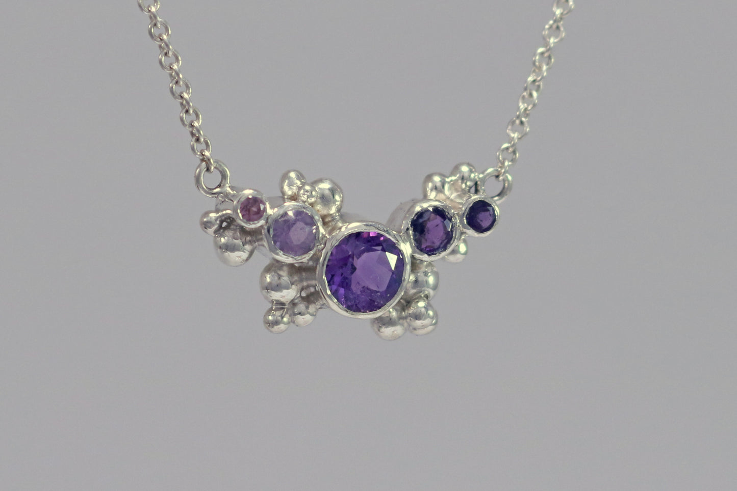 Different shades of round amethyst stones, surrounded by silver bubbles on a silver chain.
