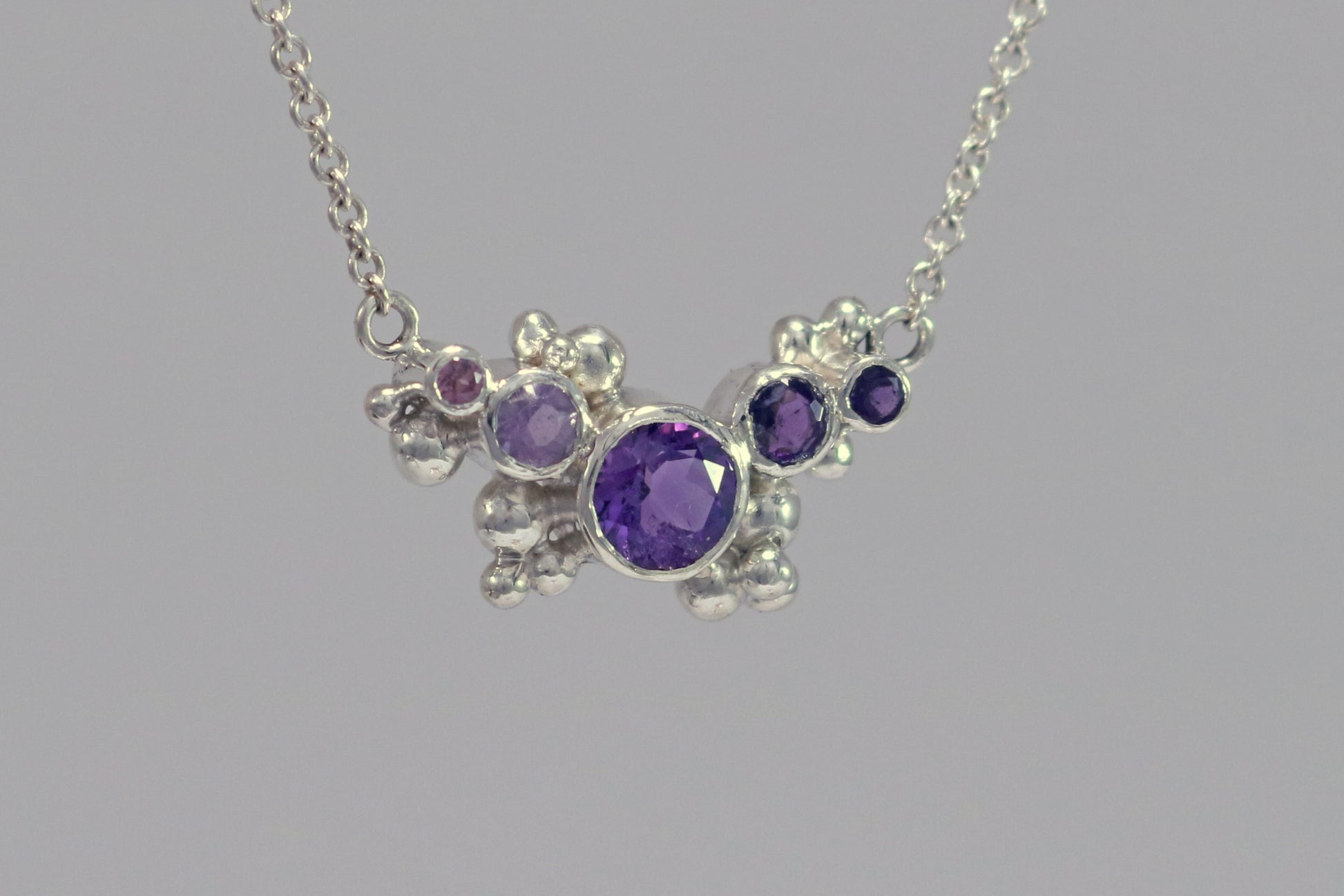 Different shades of round amethyst stones, surrounded by silver bubbles on a silver chain.