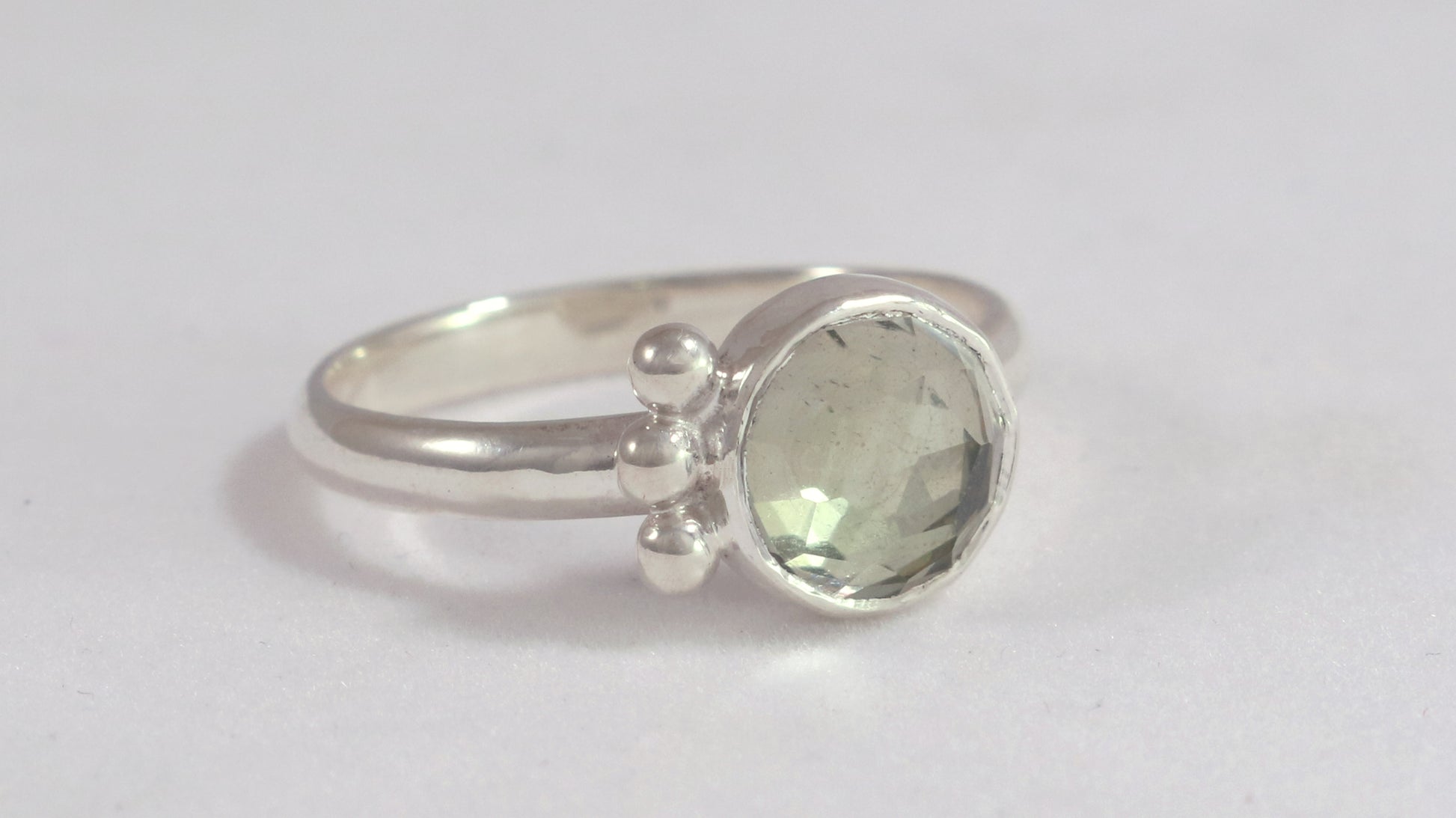 A silver ring with an 8mm round rose cut green amethyst gemstone set in sterling silver. 3 Silver bubble accents aligned along the side.