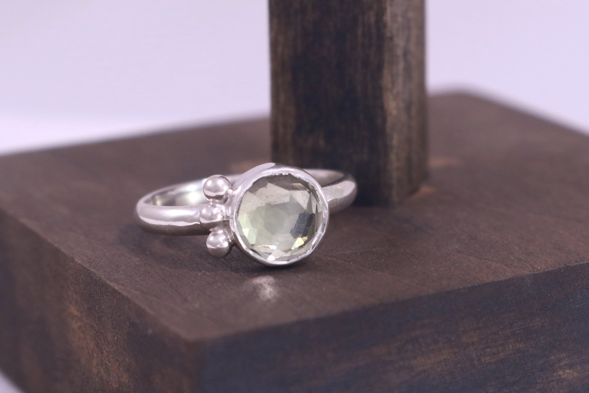 A silver ring with an 8mm round rose cut green amethyst gemstone set in sterling silver. 3 Silver bubble accents aligned along the side.