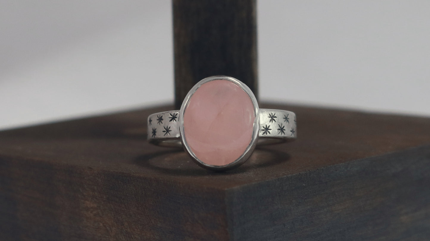 Oval natural gemstone set in sterling silver bezel on a wide sterling silver ring band with checker board of hand cut black stars on either side.