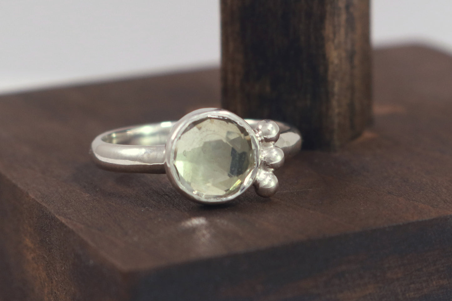 A silver ring with an 8mm round rose cut green amethyst gemstone set in sterling silver. 3 Silver bubble accents aligned along the side.