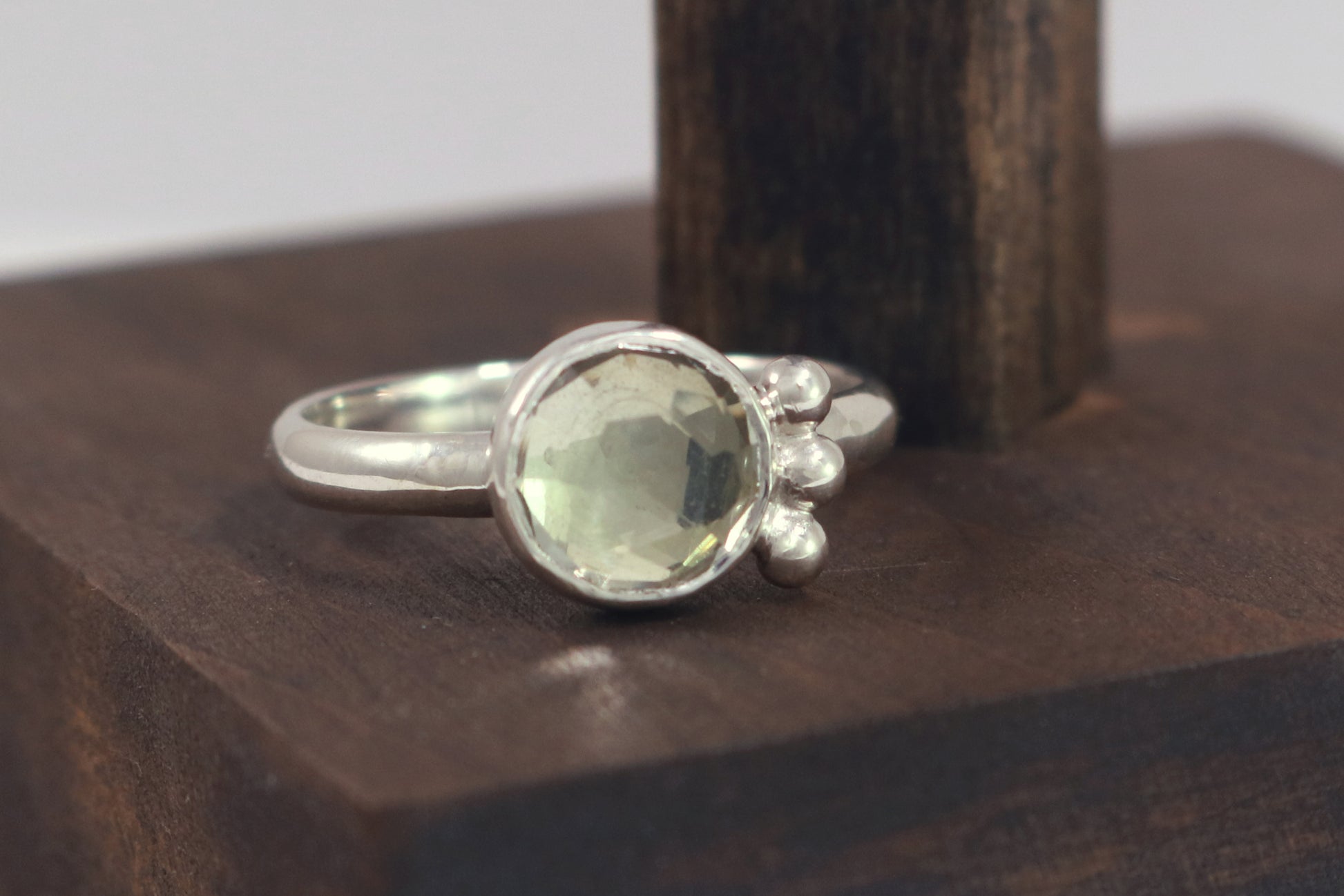 A silver ring with an 8mm round rose cut green amethyst gemstone set in sterling silver. 3 Silver bubble accents aligned along the side.