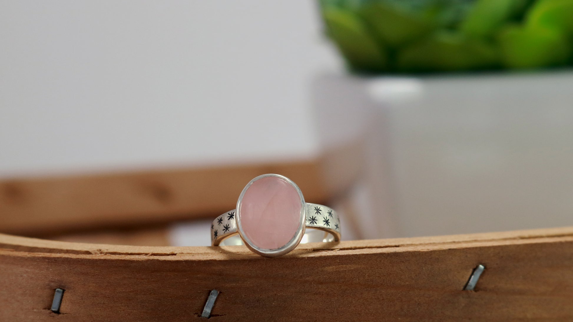 Oval natural gemstone set in sterling silver bezel on a wide sterling silver ring band with checker board of hand cut black stars on either side.
