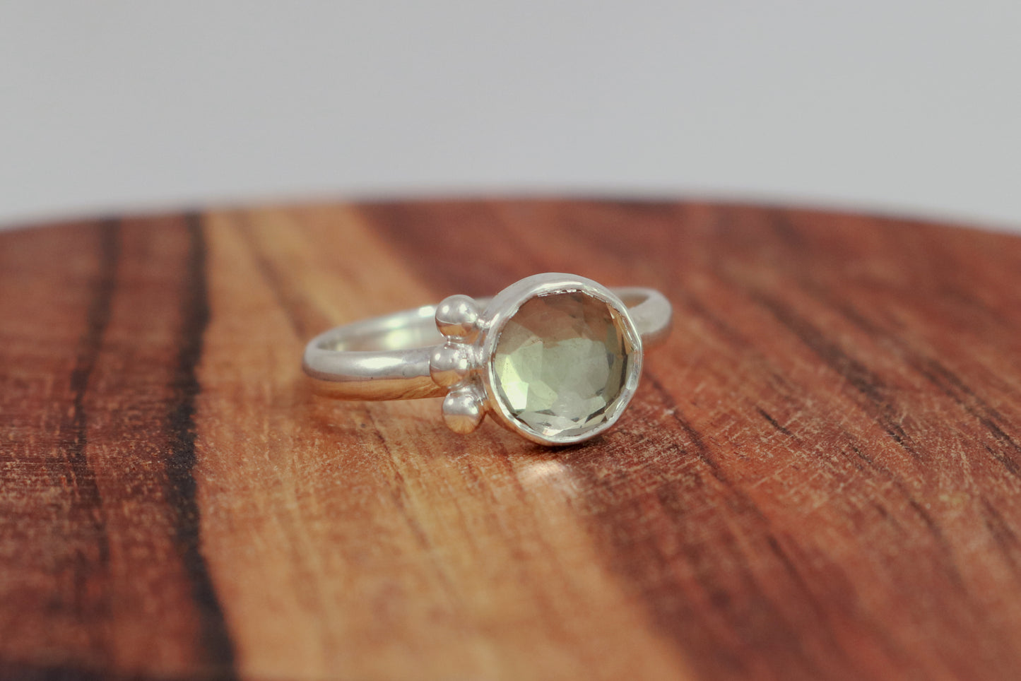 A silver ring with an 8mm round rose cut green amethyst gemstone set in sterling silver. 3 Silver bubble accents aligned along the side.