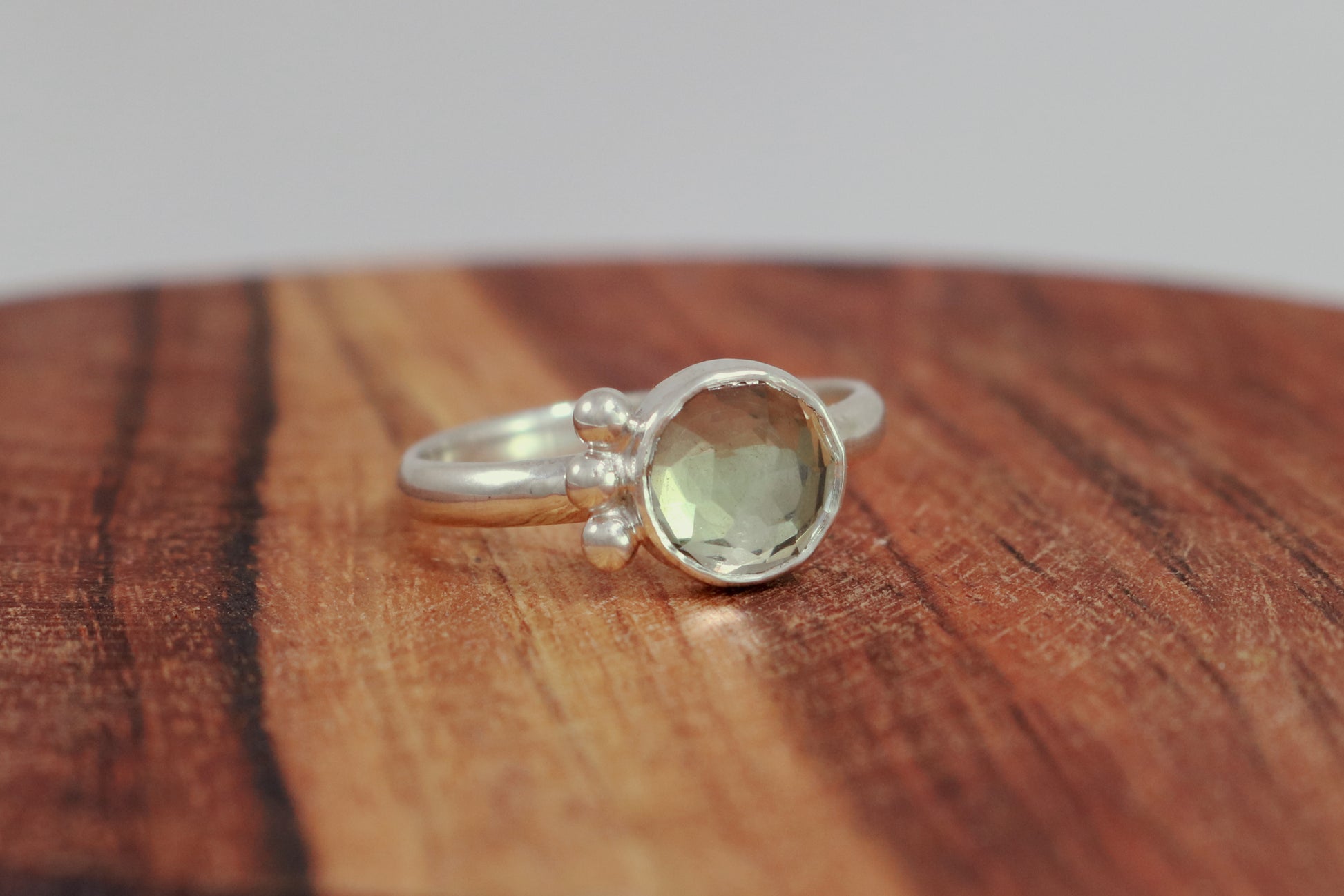 A silver ring with an 8mm round rose cut green amethyst gemstone set in sterling silver. 3 Silver bubble accents aligned along the side.