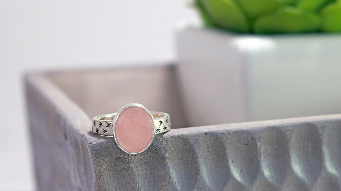 Oval natural gemstone set in sterling silver bezel on a wide sterling silver ring band with checker board of hand cut black stars on either side.