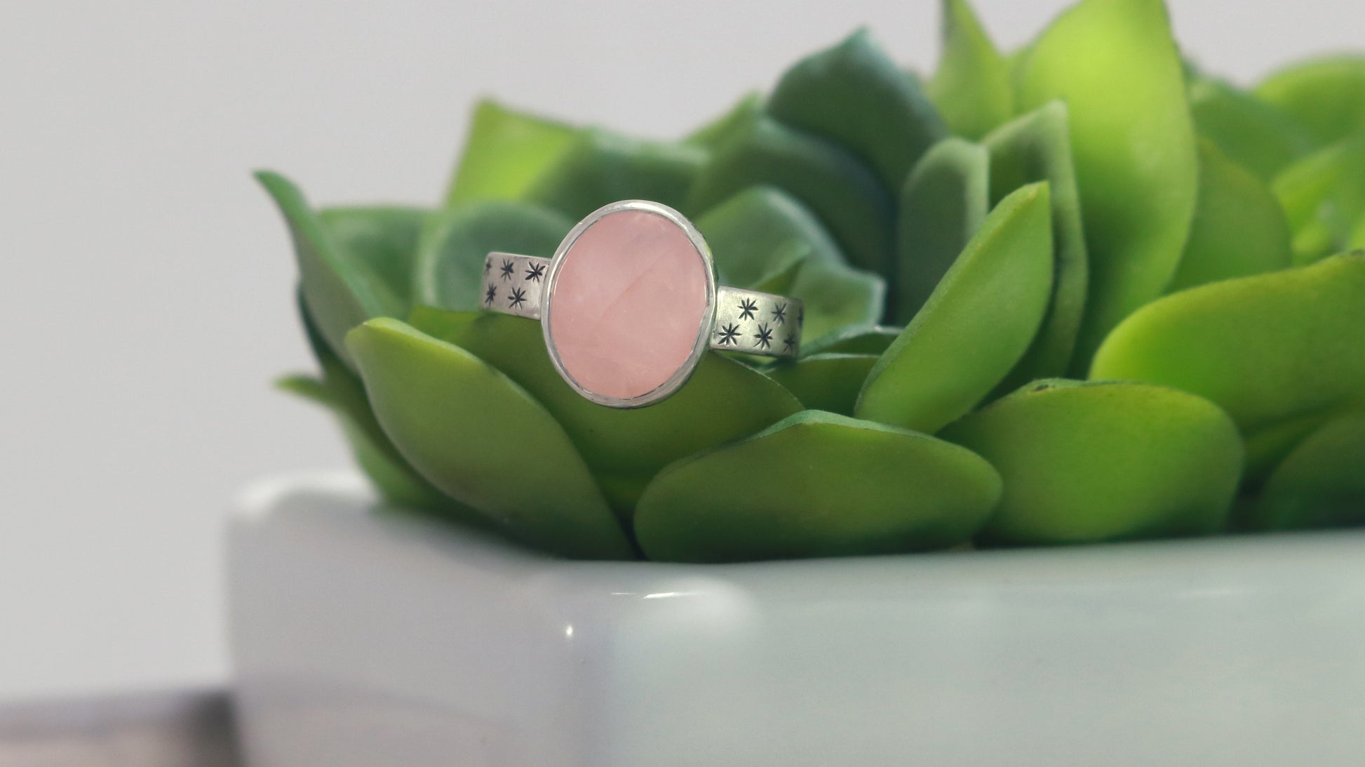 Oval natural gemstone set in sterling silver bezel on a wide sterling silver ring band with checker board of hand cut black stars on either side.