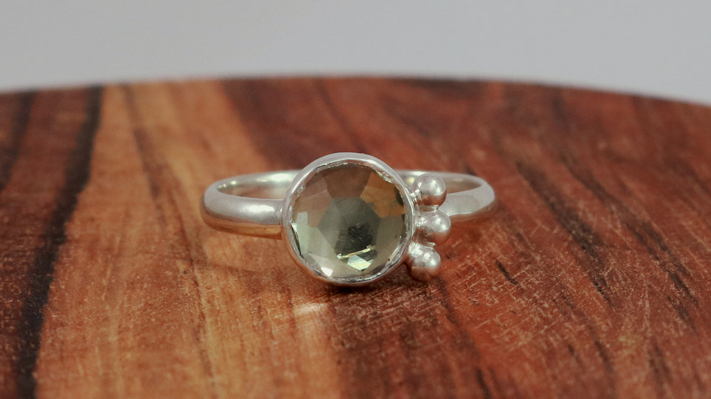 A silver ring with an 8mm round rose cut green amethyst gemstone set in sterling silver. 3 Silver bubble accents aligned along the side.