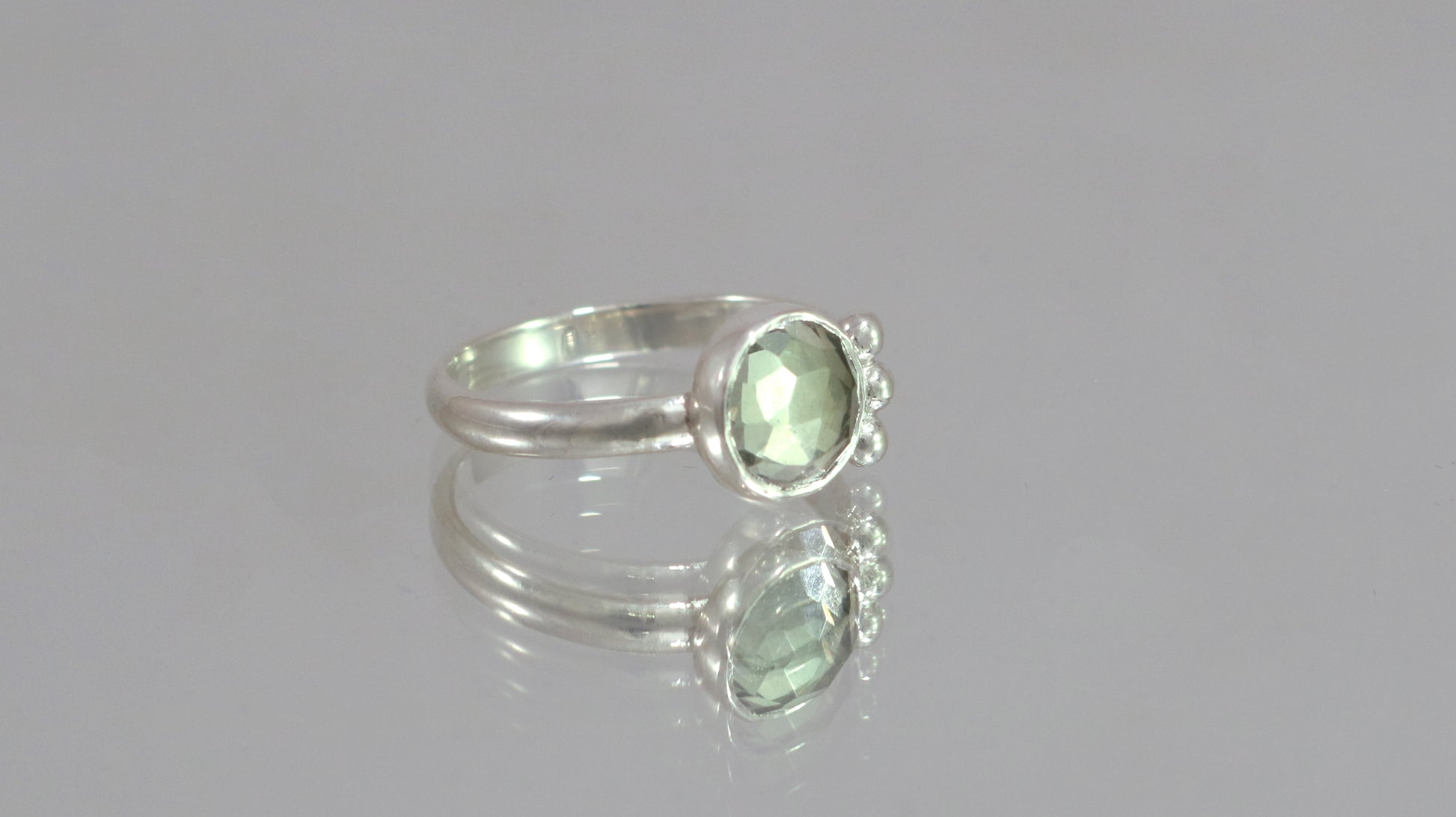 A silver ring with an 8mm round rose cut green amethyst gemstone set in sterling silver. 3 Silver bubble accents aligned along the side.