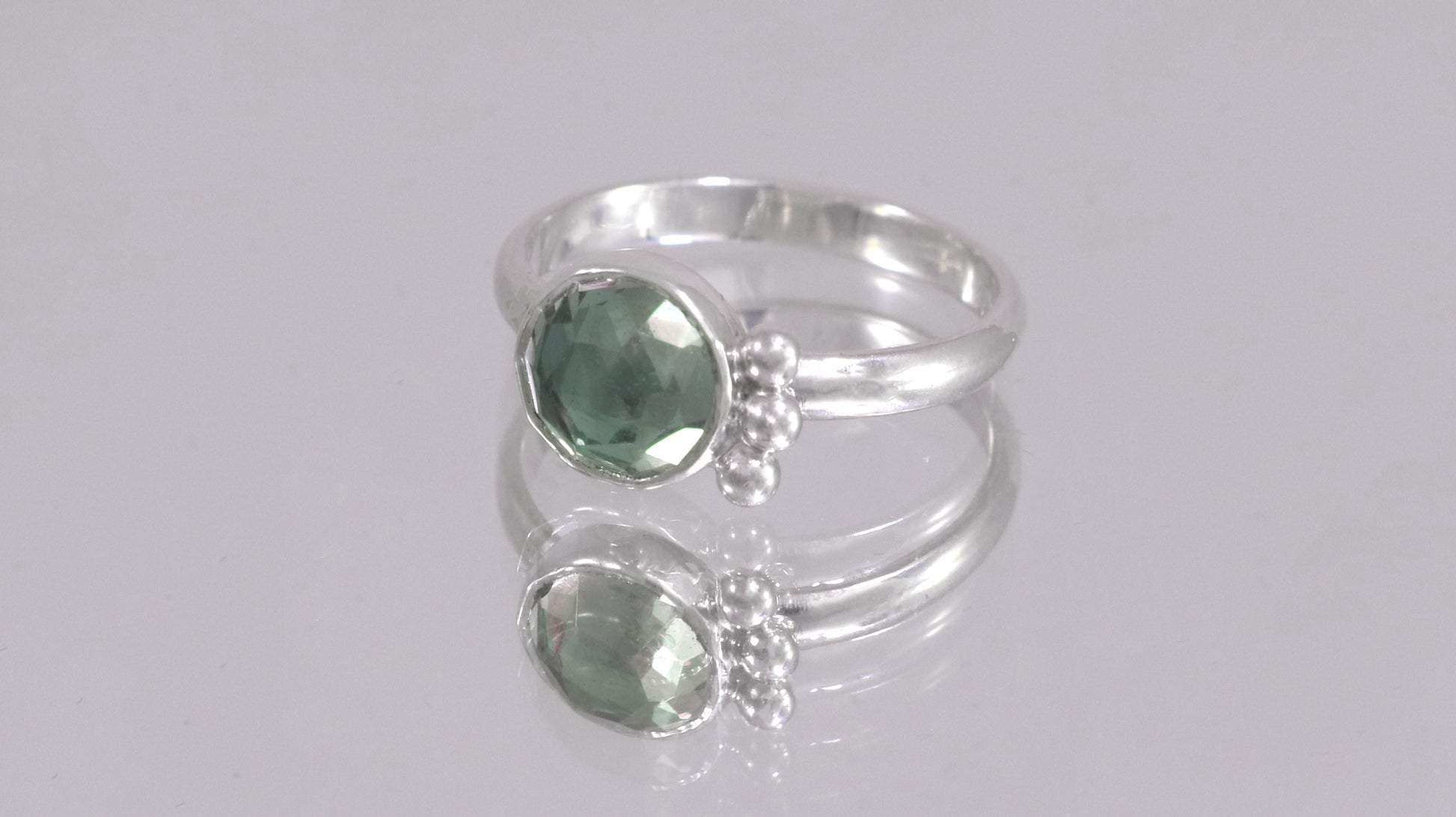A silver ring with an 8mm round rose cut green amethyst gemstone set in sterling silver. 3 Silver bubble accents aligned along the side.
