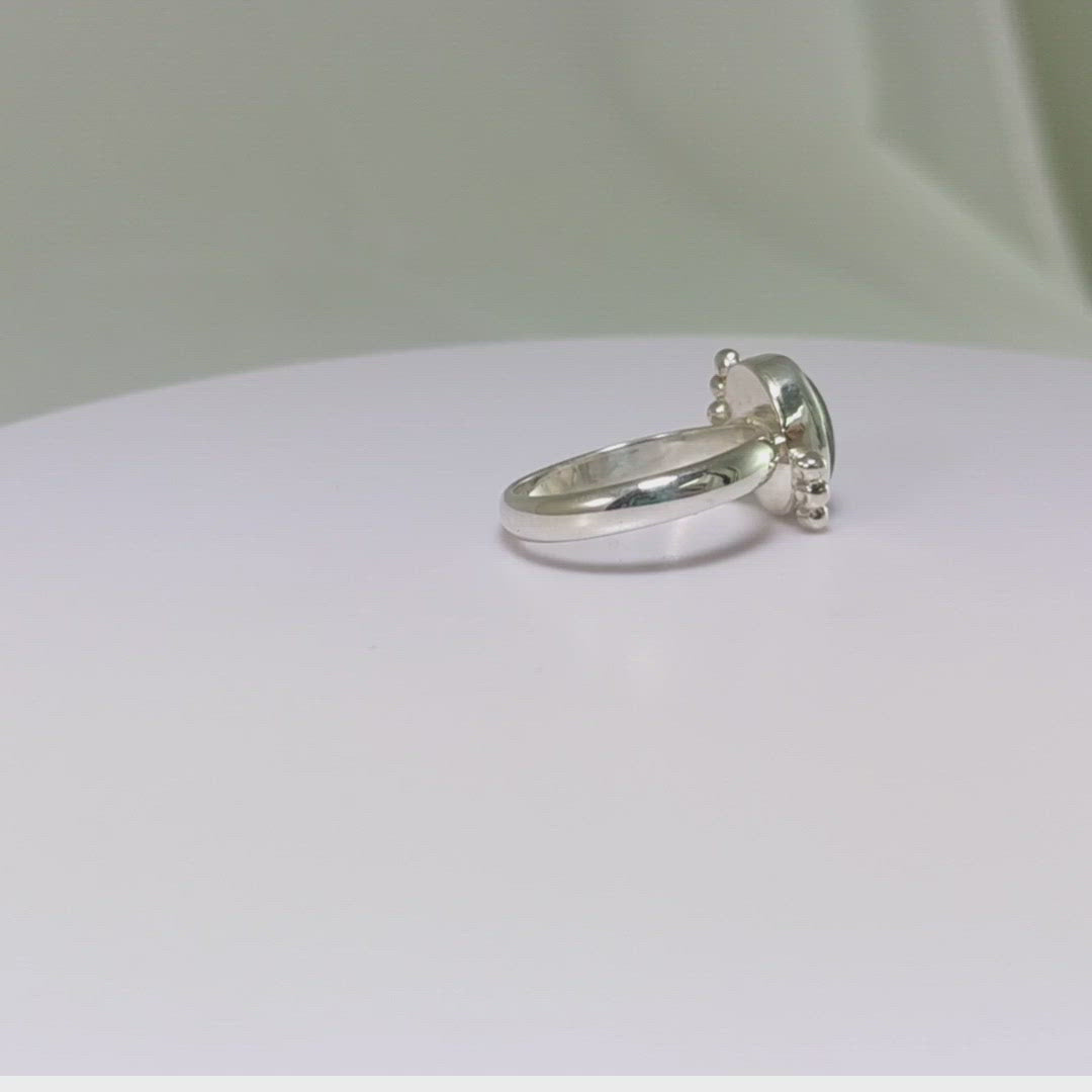 A royal blue, oval labradorite stone is bezel set on a sterling silver ring. On opposite diagonals are three silver bubbles with a total of 6 bubbles on the stone.