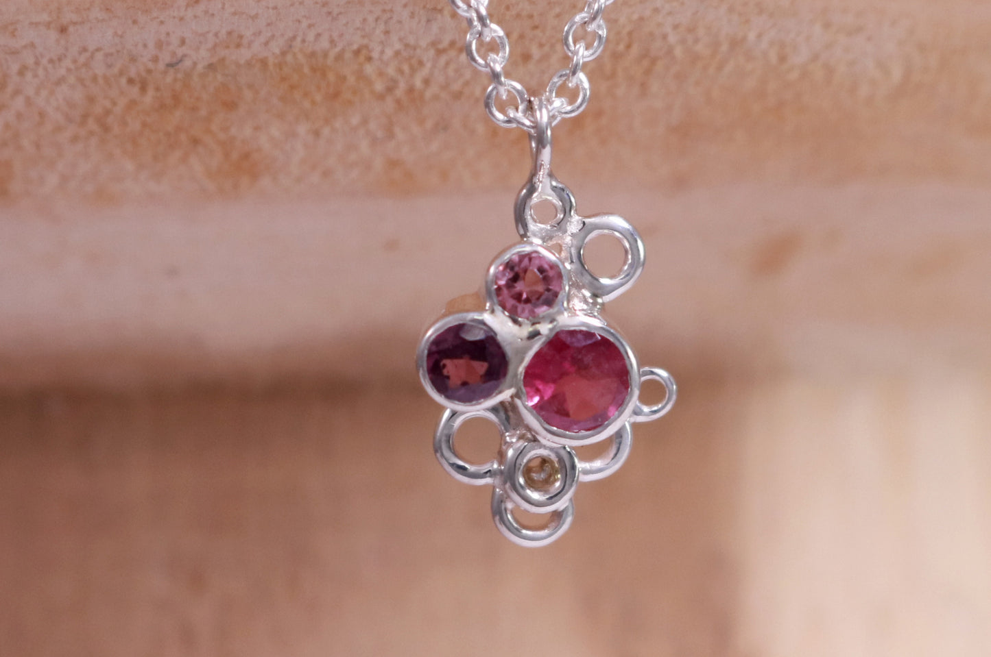 Three pink gemstones of descending sizes set in sterling silver bezels, grouped together in the shape of a triangle. Around the triangle are open silver circles. The pendant hangs on a sterling silver chain.