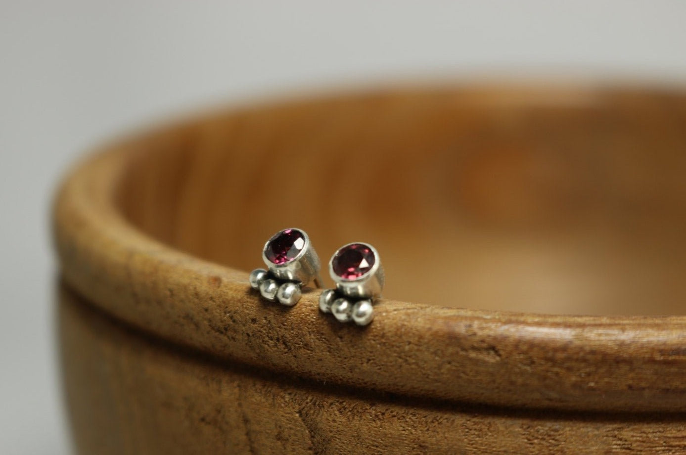 A pair of deep pink, round, faceted rhodolites set in sterling silver bezels with three silver bubbles aligned along the bezel.