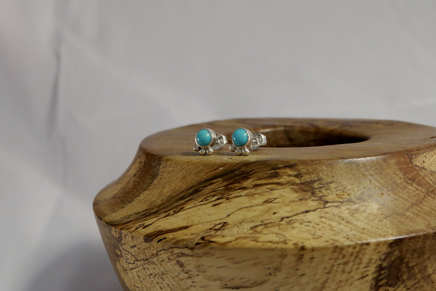 A pair of 5mm, round turquoise stones set in sterling silver with three silver bubbles aligned along the bezel.