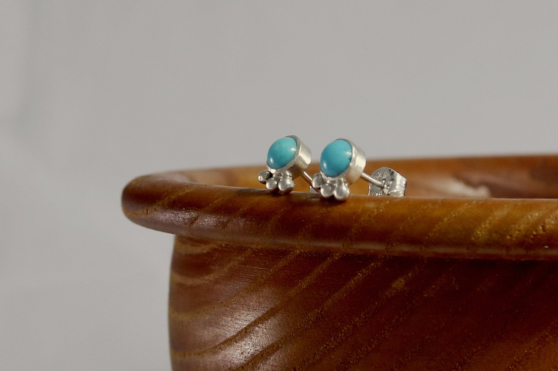 A pair of 5mm, round turquoise stones set in sterling silver with three silver bubbles aligned along the bezel.