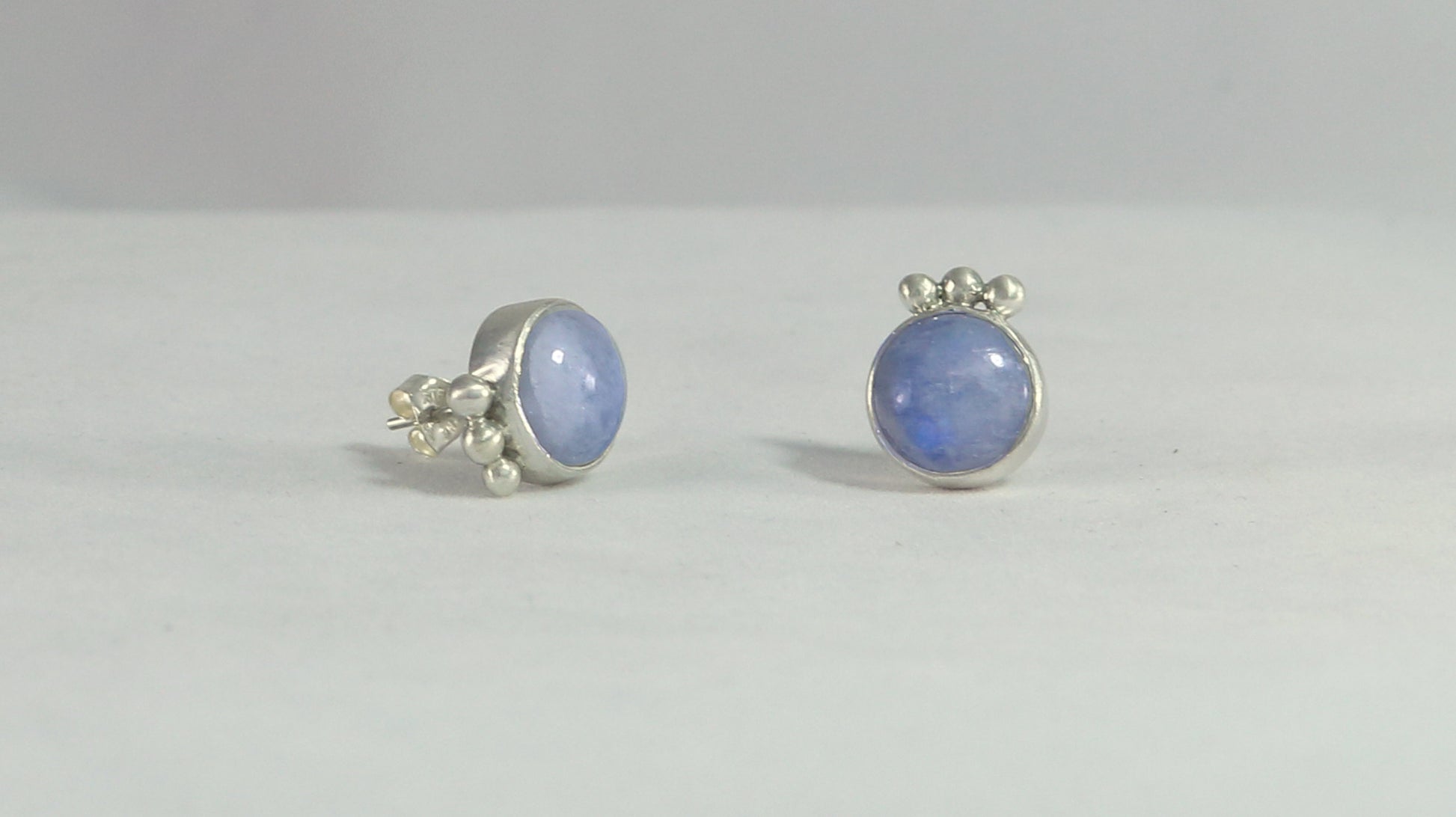 A pair of round rainbow moonstone stud earrings with 3 silver bubbles in a row at the bottom.