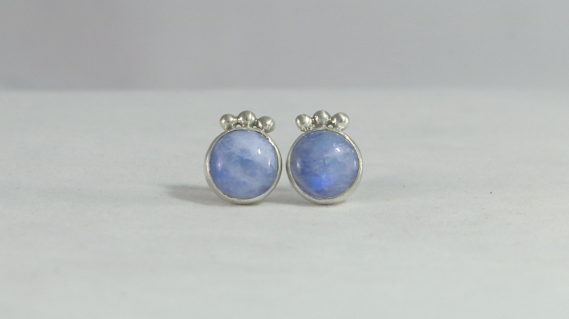 A pair of round rainbow moonstone stud earrings with 3 silver bubbles in a row at the top.