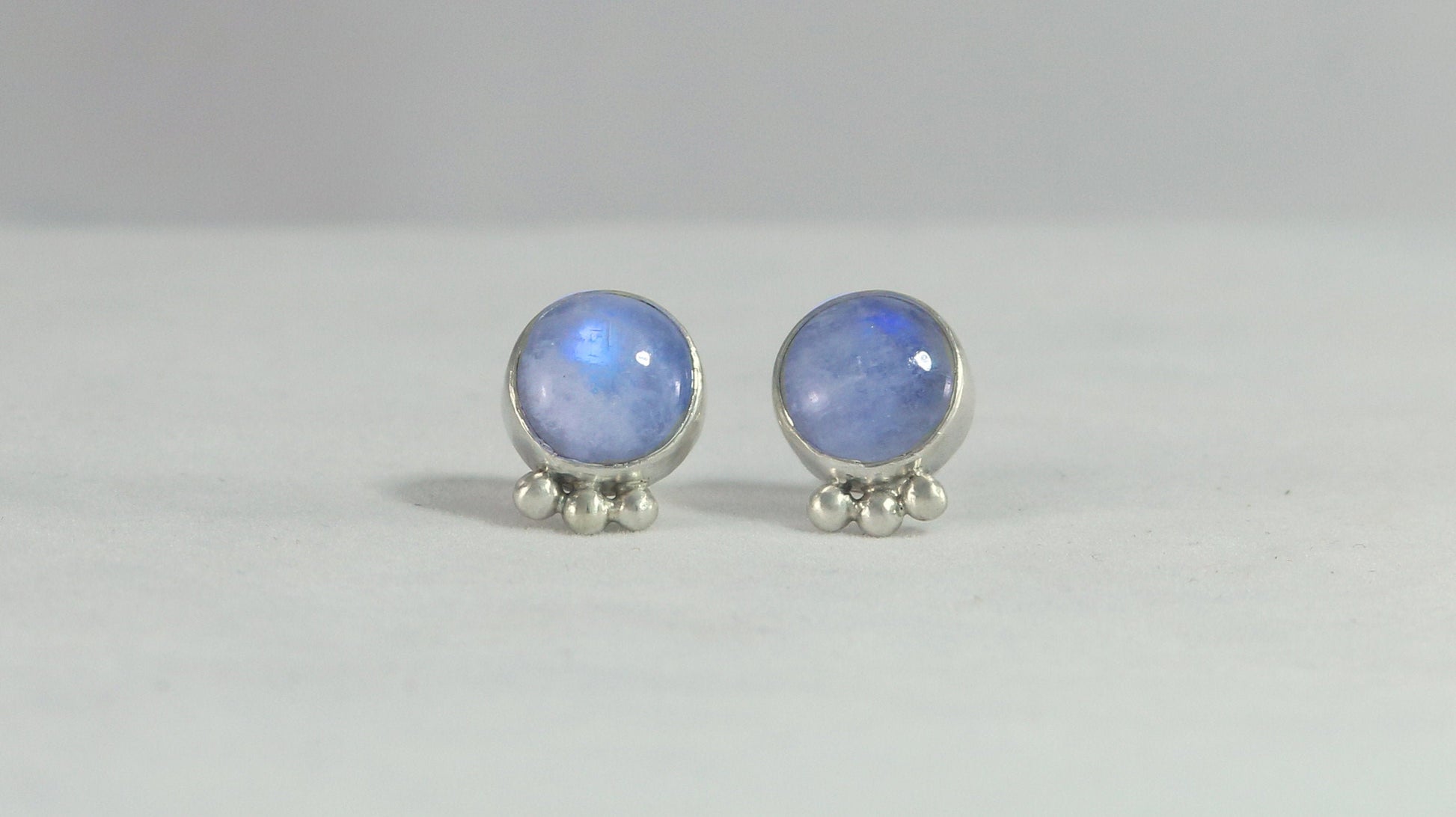 A pair of round rainbow moonstone stud earrings with 3 silver bubbles in a row at the bottom.