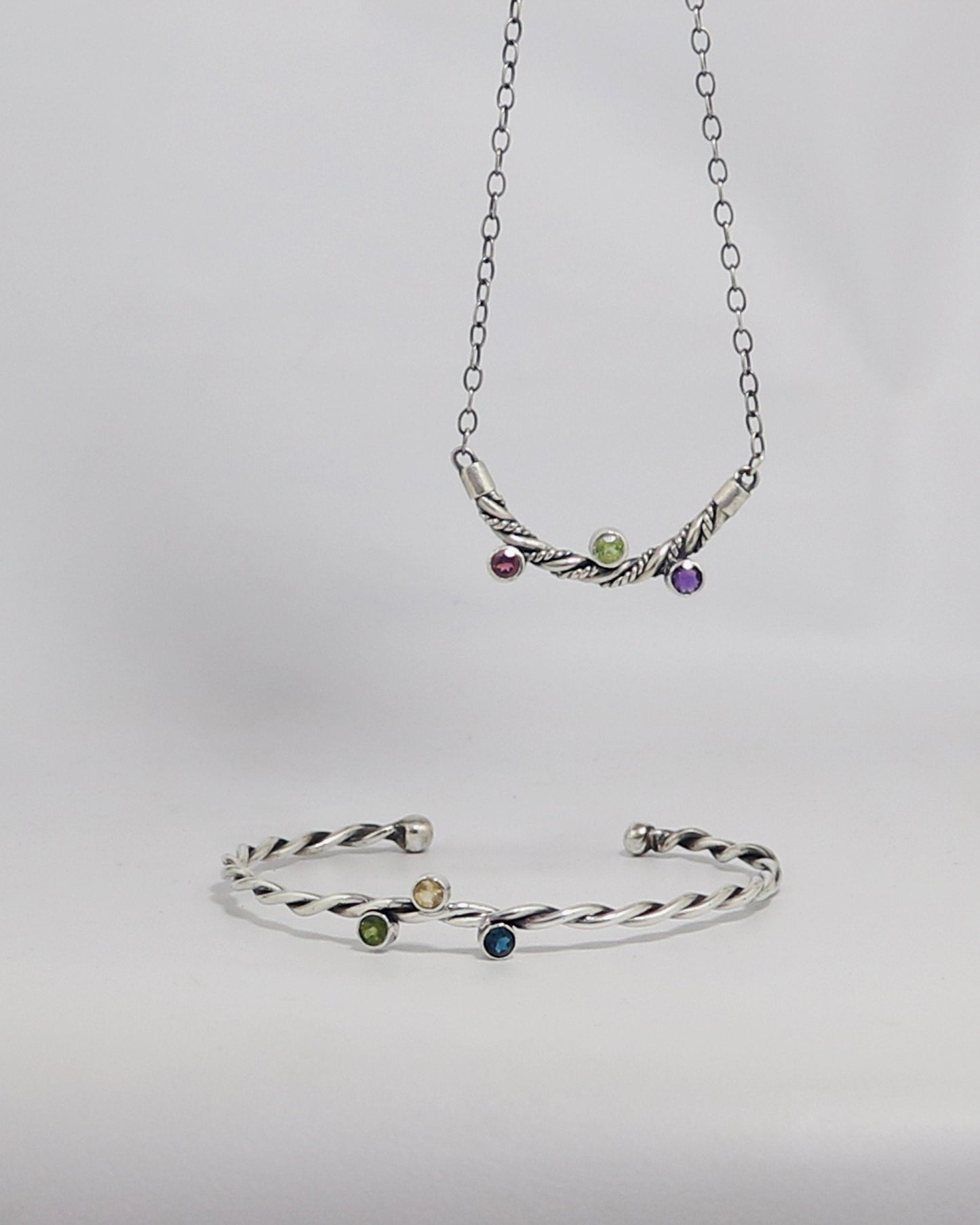 Curved solid sterling silver twisted pendant with 3 bezel set gemstones photographed with matching cuff.