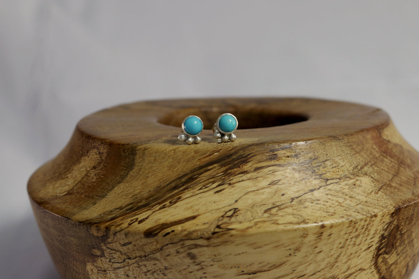 A pair of 5mm, round turquoise stones set in sterling silver with three silver bubbles aligned along the bezel.