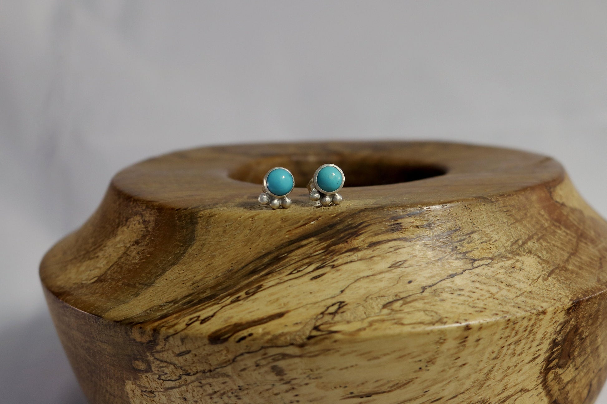 A pair of 5mm, round turquoise stones set in sterling silver with three silver bubbles aligned along the bezel.