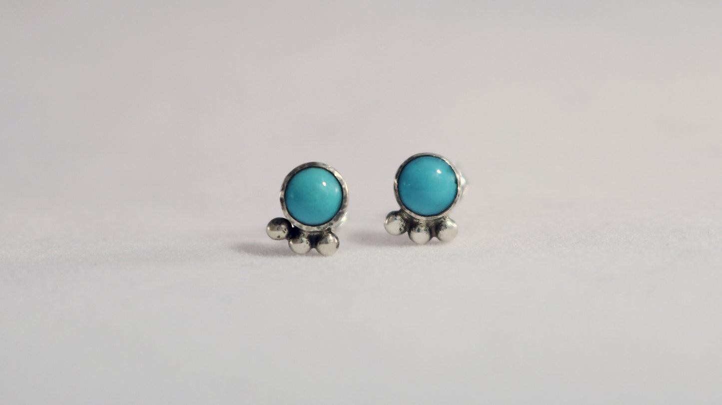 A pair of 5mm, round turquoise stones set in sterling silver with three silver bubbles aligned along the bezel.