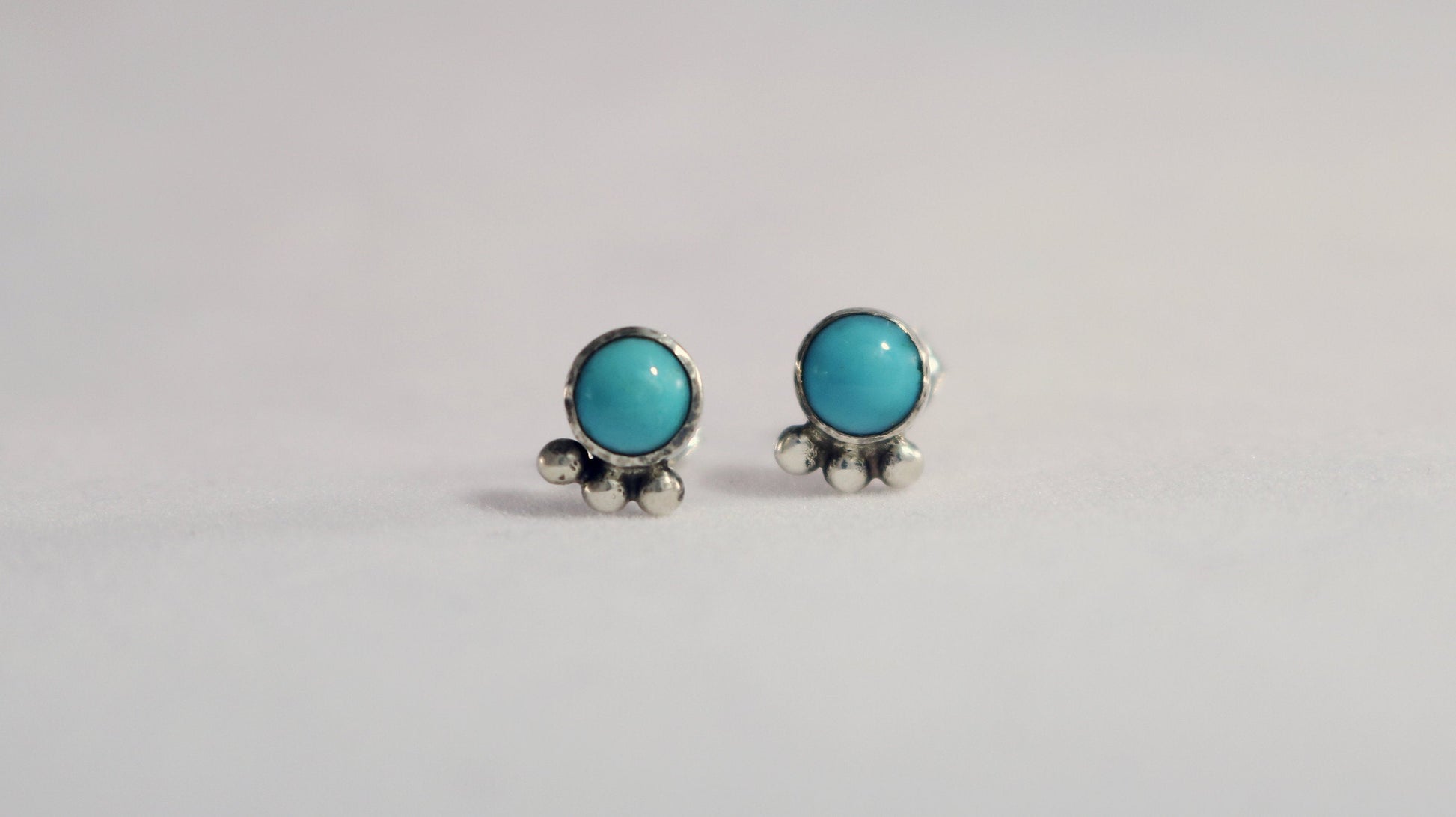 A pair of 5mm, round turquoise stones set in sterling silver with three silver bubbles aligned along the bezel.