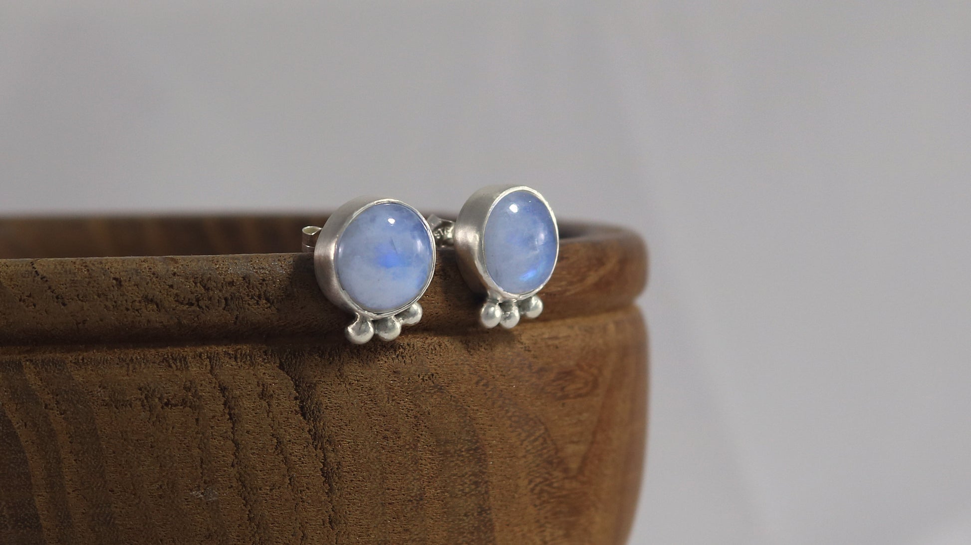 A pair of round rainbow moonstone stud earrings with 3 silver bubbles in a row at the bottom.