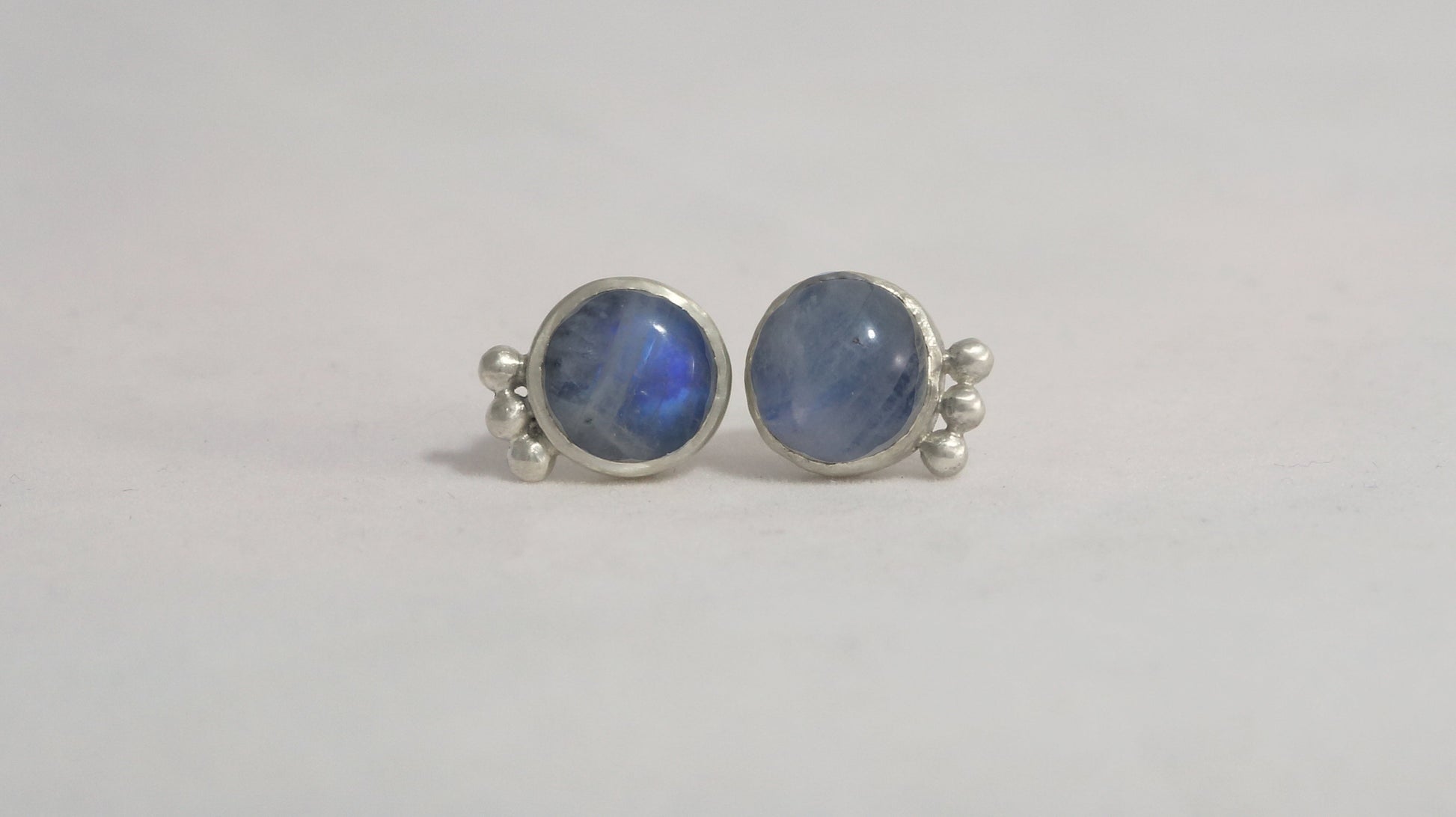 A pair of round rainbow moonstone stud earrings with 3 silver bubbles in a row at the bottom.