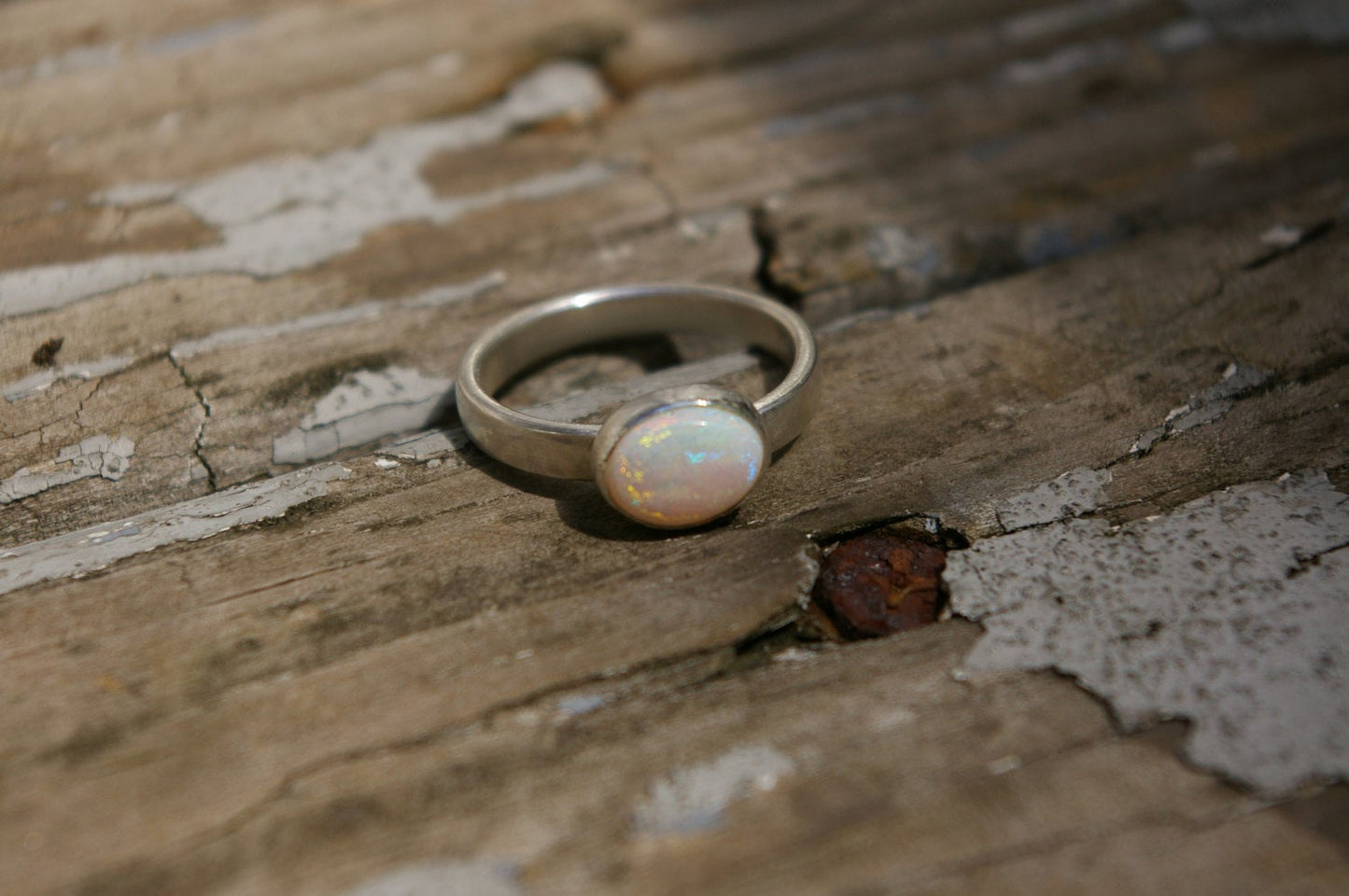 Oval natural white opal set in sterling silver bezel on a sterling silver ring band.