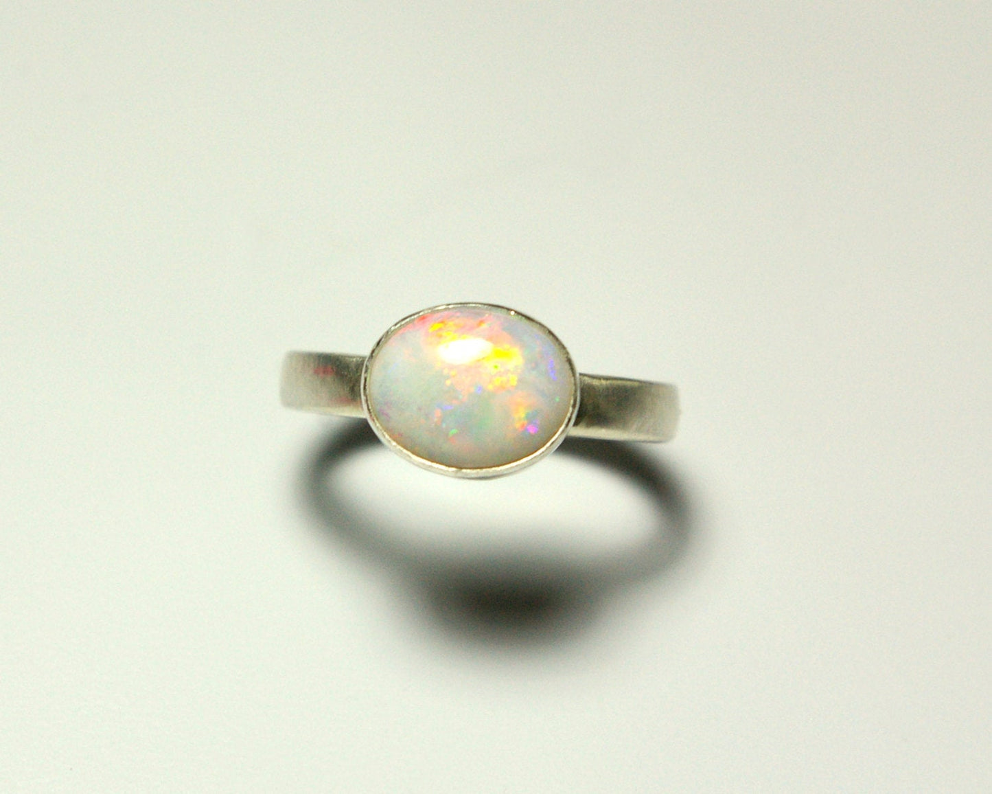 Oval natural white opal set in sterling silver bezel on a sterling silver ring band.