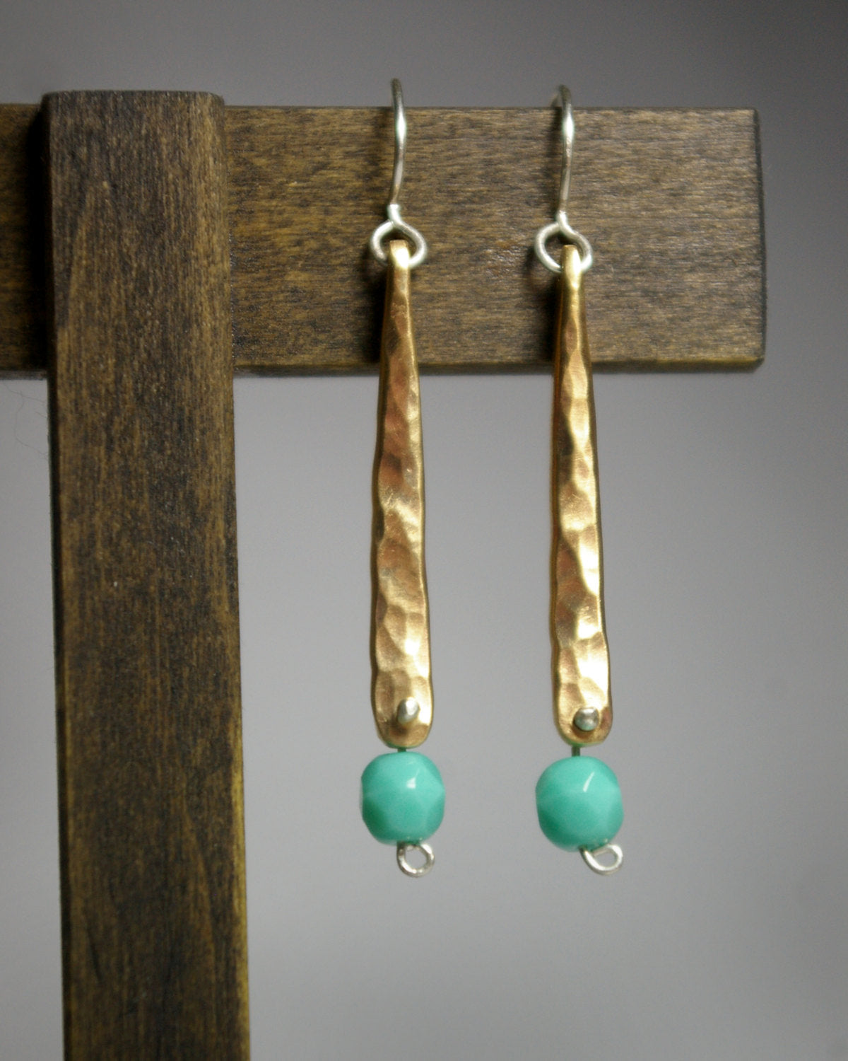 A hand forged, textured, brass, elongated drop with a hanging glass turquoise colored bead.