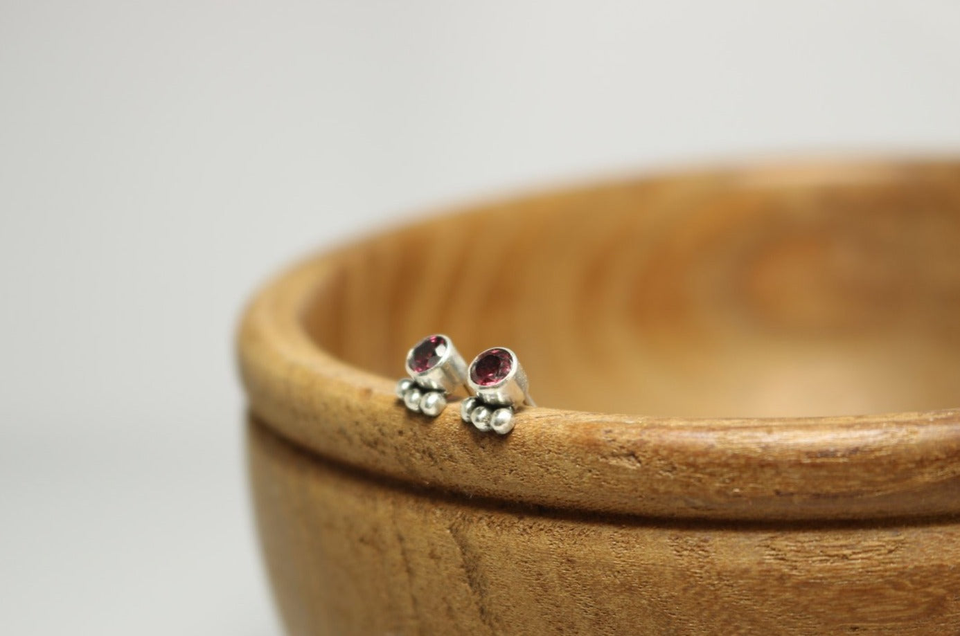 A pair of deep pink, round, faceted rhodolites set in sterling silver bezels with three silver bubbles aligned along the bezel.