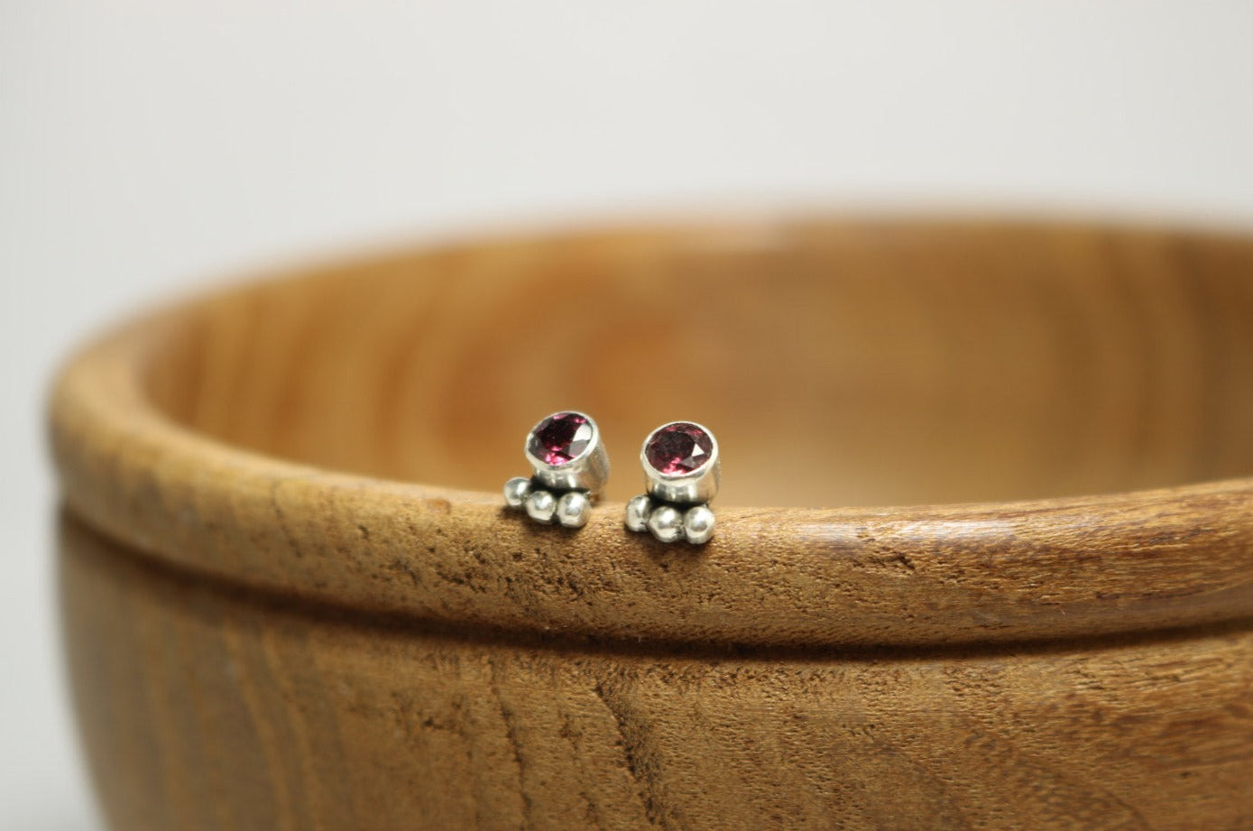 A pair of deep pink, round, faceted rhodolites set in sterling silver bezels with three silver bubbles aligned along the bezel.