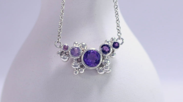 Different shades of round amethyst stones, surrounded by silver bubbles on a silver chain.
