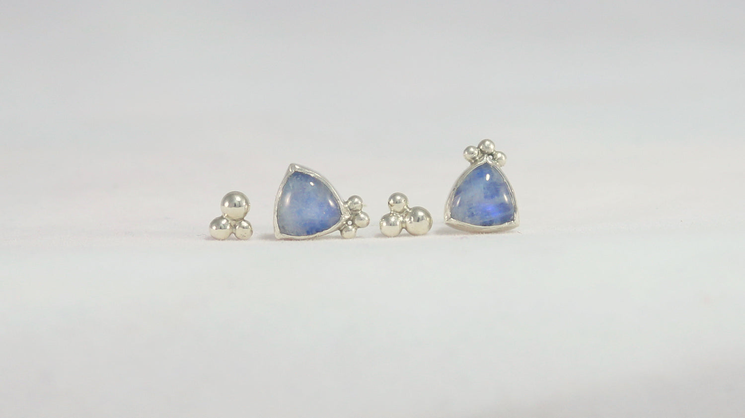 2 pairs of stud earrings. One pair is 3 silver bubbles decreasing in size shaped like a pyramid. The other pair is trillion rainbow moonstones with three bubbles on one of the points.