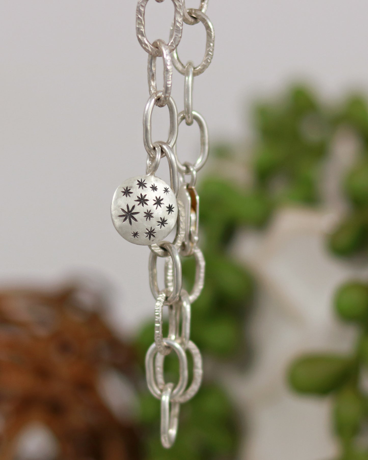 Handmade out of sterling silver, this oval chain link bracelet features a handmade sterling silver charm with hand carved stars.