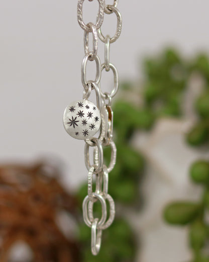 Handmade out of sterling silver, this oval chain link bracelet features a handmade sterling silver charm with hand carved stars.