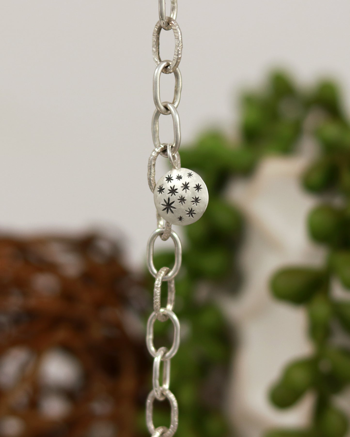 Handmade out of sterling silver, this oval chain link bracelet features a handmade sterling silver charm with hand carved stars.