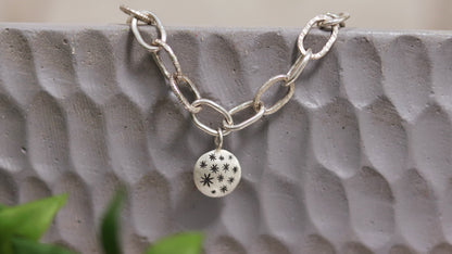 Handmade out of sterling silver, this oval chain link bracelet features a handmade sterling silver charm with hand carved stars.