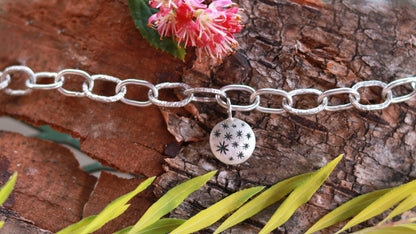 Handmade out of sterling silver, this oval chain link bracelet features a handmade sterling silver charm with hand carved stars.