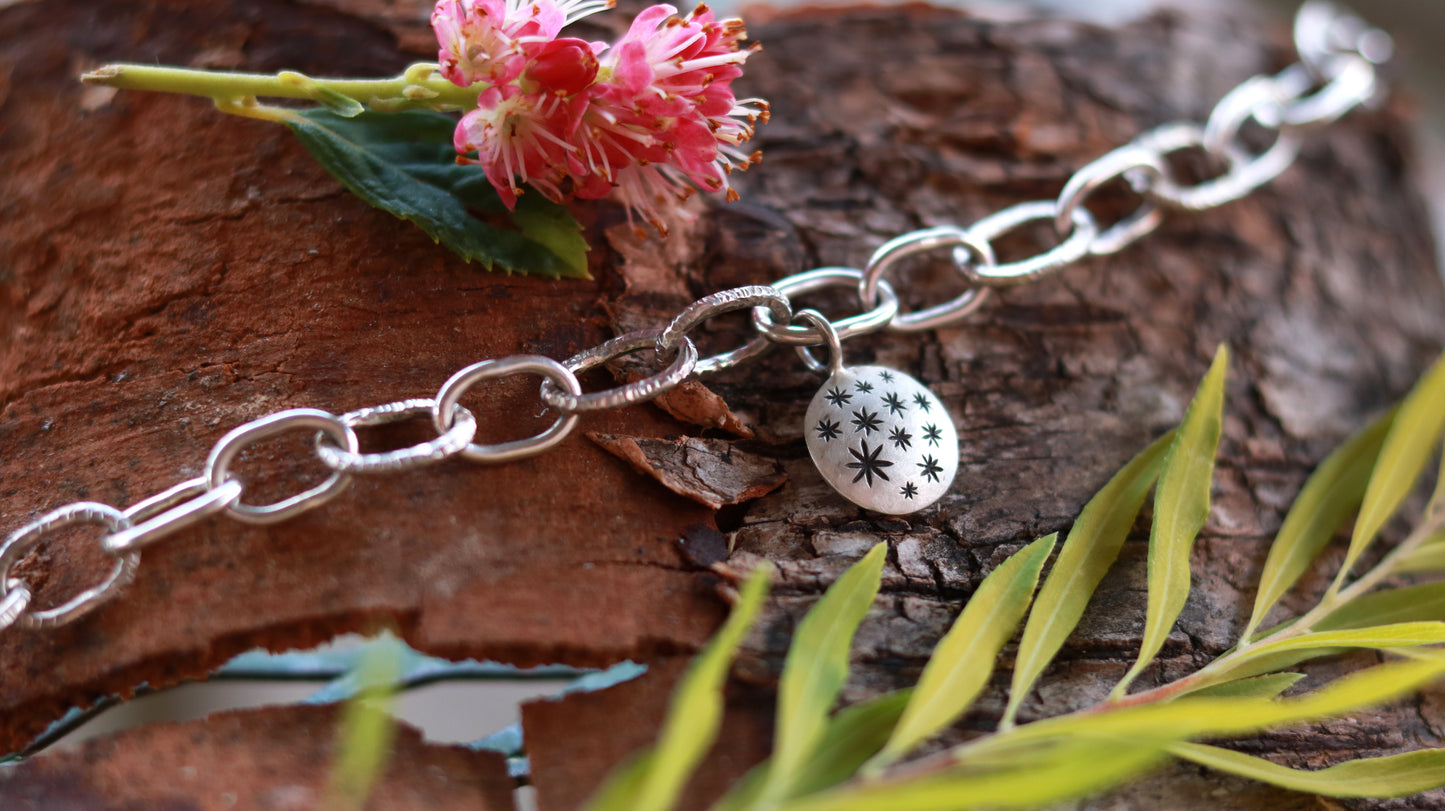 Handmade out of sterling silver, this oval chain link bracelet features a handmade sterling silver charm with hand carved stars.