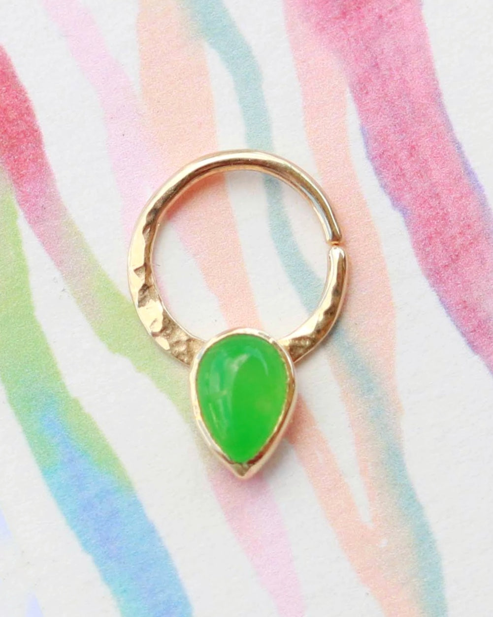 A 14k yellow gold septum hoop with a pear shaped jade gemstone that is bezel set, pointing downwards. The metal on the hoop has been textured and the entire piece is polished.