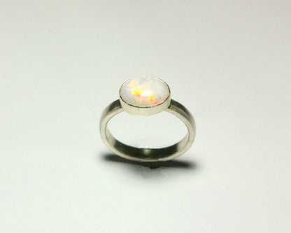 Oval natural white opal set in sterling silver bezel on a sterling silver ring band.