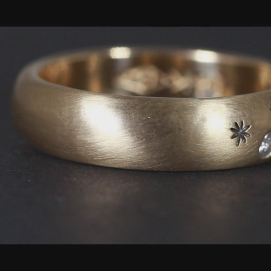 A rounded yellow gold ring band with hand carved, black stars sprinkled between 3 bright white full cut diamonds that are flush set into the gold.