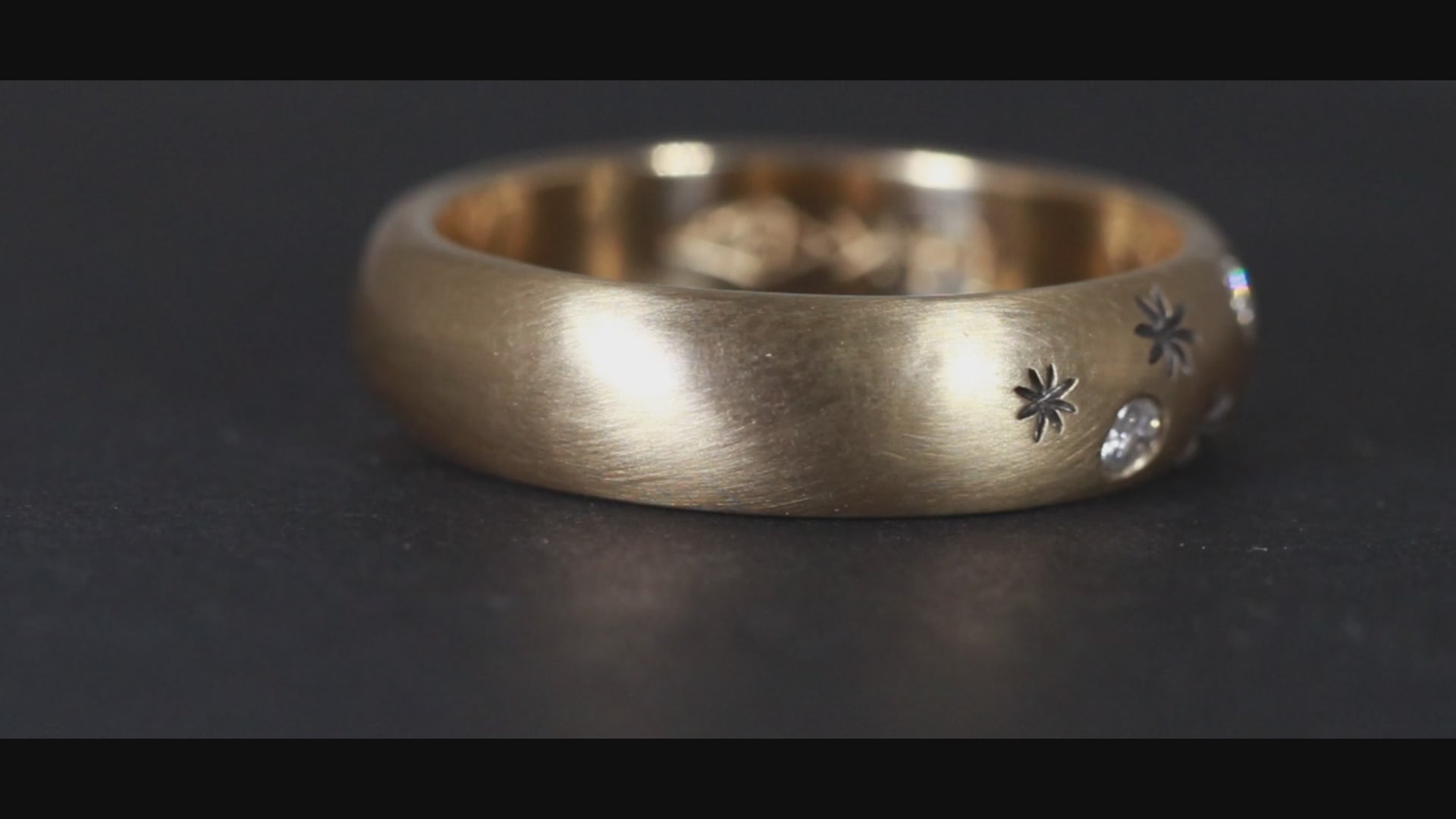 A rounded yellow gold ring band with hand carved, black stars sprinkled between 3 bright white full cut diamonds that are flush set into the gold.