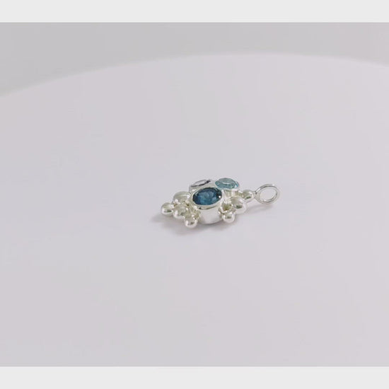 A video of a pendant on a silver chain, three round gemstones, all a different shade of blue, set in a pyramid shape with randomly placed silver bubbles.