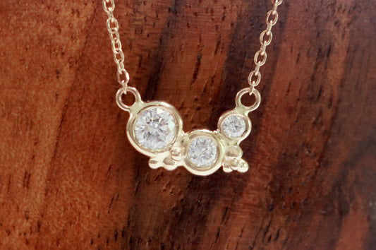 Three diamonds of descending size are set in 14k yellow gold bezels with little bubble clusters at the bottoms.